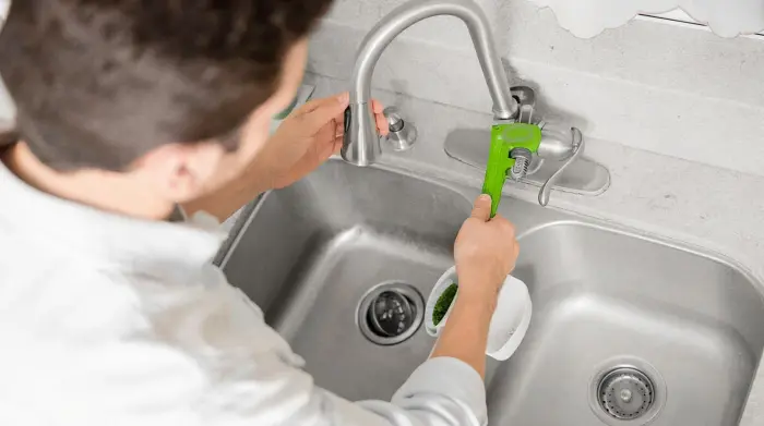 Hands loosening a kitchen faucet handle with a wrench