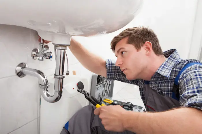 Plumber tightening the trap under a bathroom sink with pliers