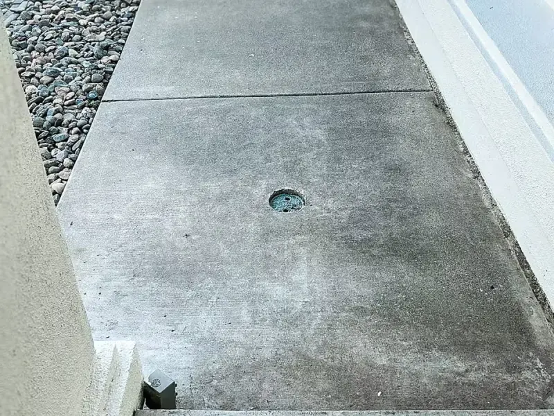 Sewer cleanout in a concrete side walkway next to a house