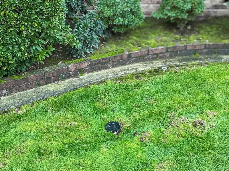Sewer cleanout cap in a front lawn below a brick planter bed