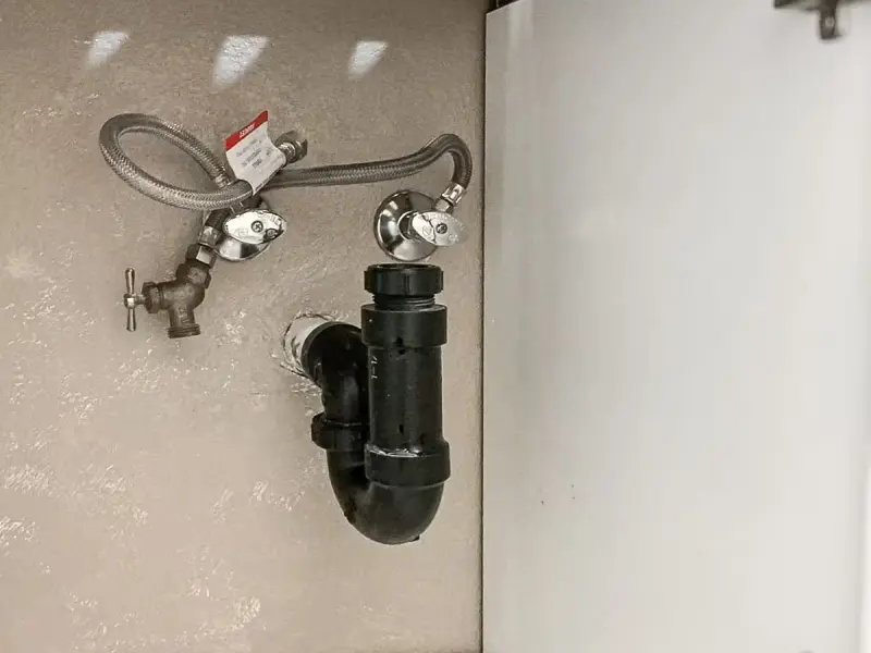 New angle stop valves, braided supply line and black drain trap inside a sink cabinet