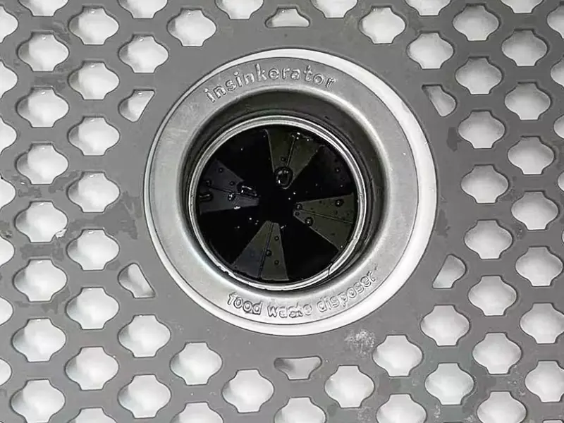 InSinkErator disposal opening seen through a gray sink grid after drain maintenance