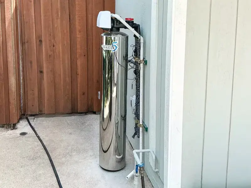 Stainless steel whole-house water filtration tank installed along a side yard wall