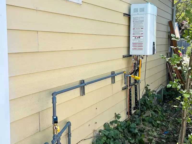 Outdoor tankless water heater on yellow siding with a new gas line run from the meter