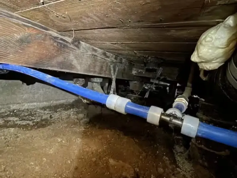 New blue PEX water line run beneath the floor joists in a crawlspace