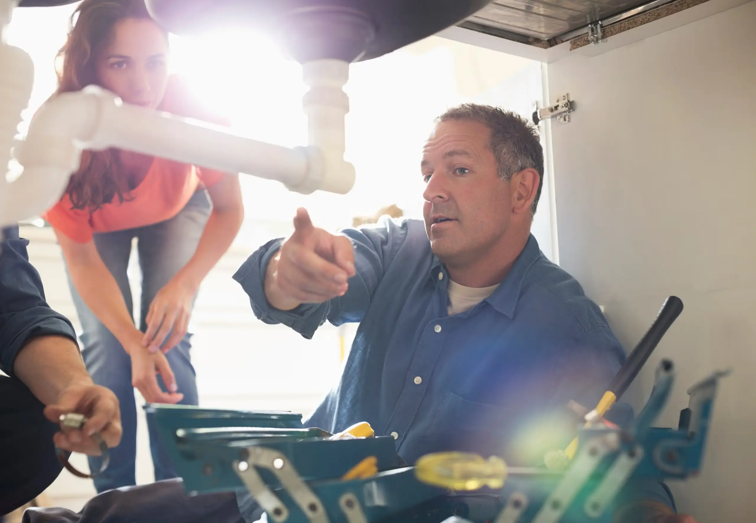 Two people working on the plumbing under a kitchen sink — Beaver Brothers Plumbing