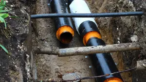 Old sewer pipe exposed in a trench beside a new black replacement pipe